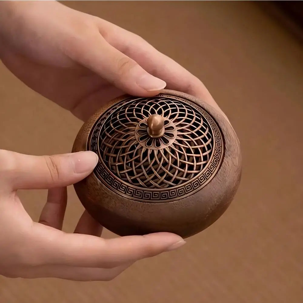 Close-up of a person's hands holding the Heritage round solid wood incense burner with its geometric brass lattice lid attached, showcasing its tactile quality and compact scale.