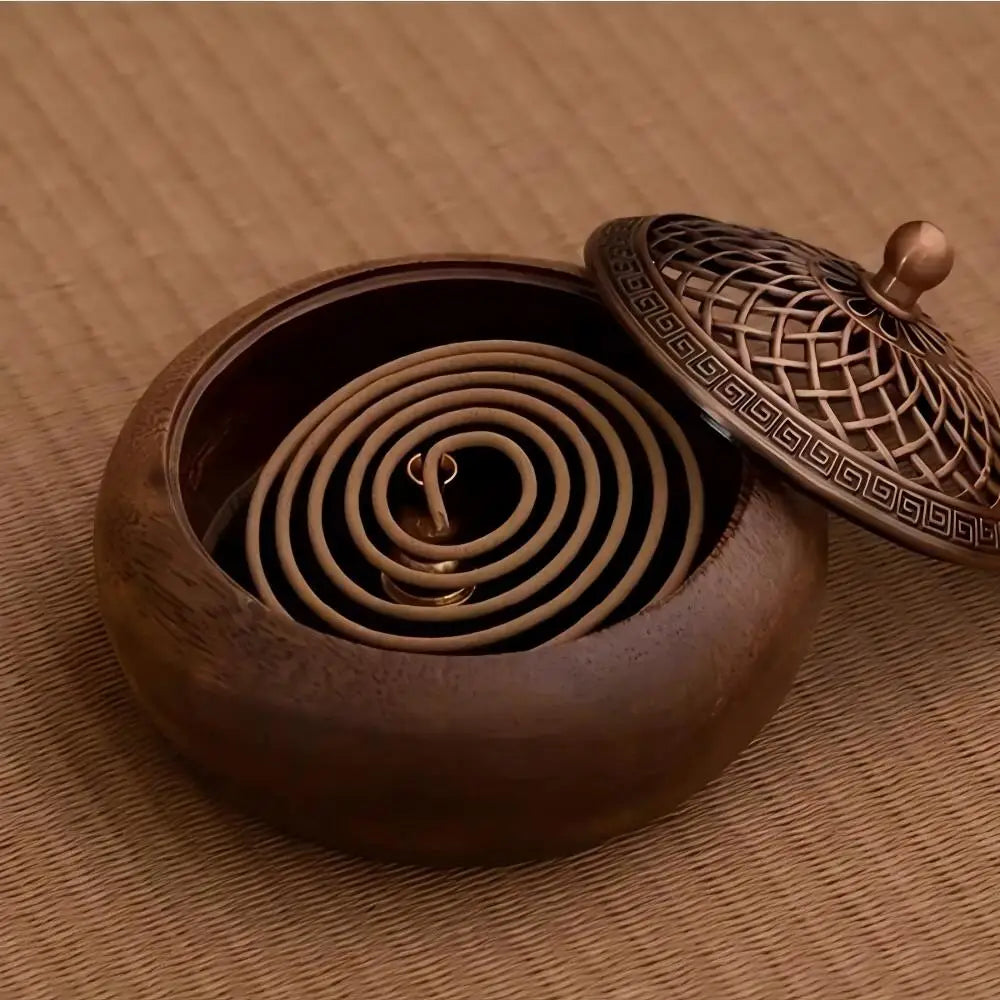 An open wooden incense bowl on a textured woven mat, displaying an active aromatherapy incense coil resting inside on a safe fireproof pad.