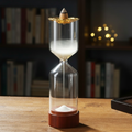 The Hourglass Waterfall Incense Vessel gracefully streaming white smoke into its lower glass chamber, resting on a wooden desk with a blurred bookshelf and warm fairy lights in the background.