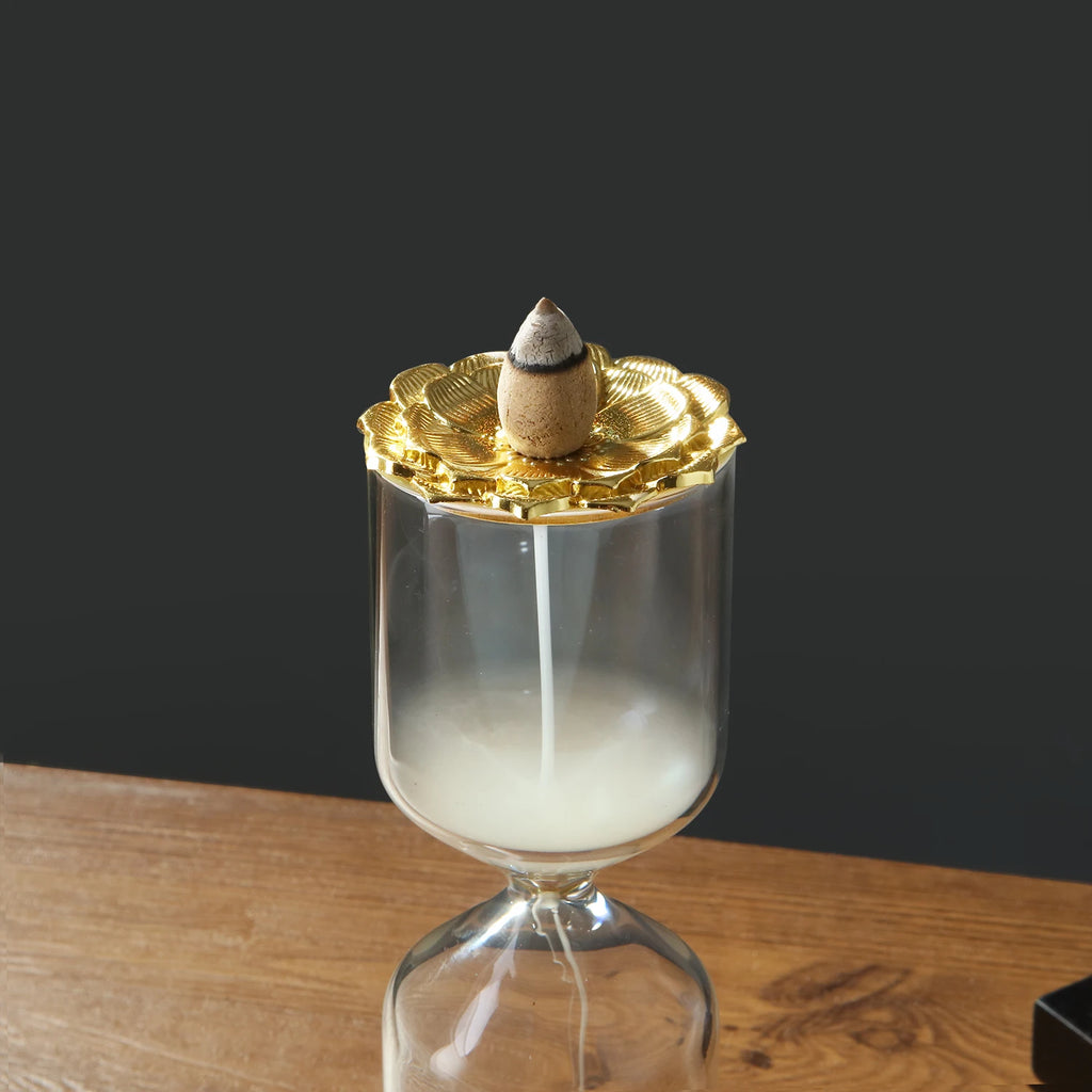 The Hourglass Waterfall Incense Vessel standing upright on a wooden table against a minimalist dark grey background, showing mesmerizing white smoke pooling in the top glass section and dripping down into the bottom chamber.