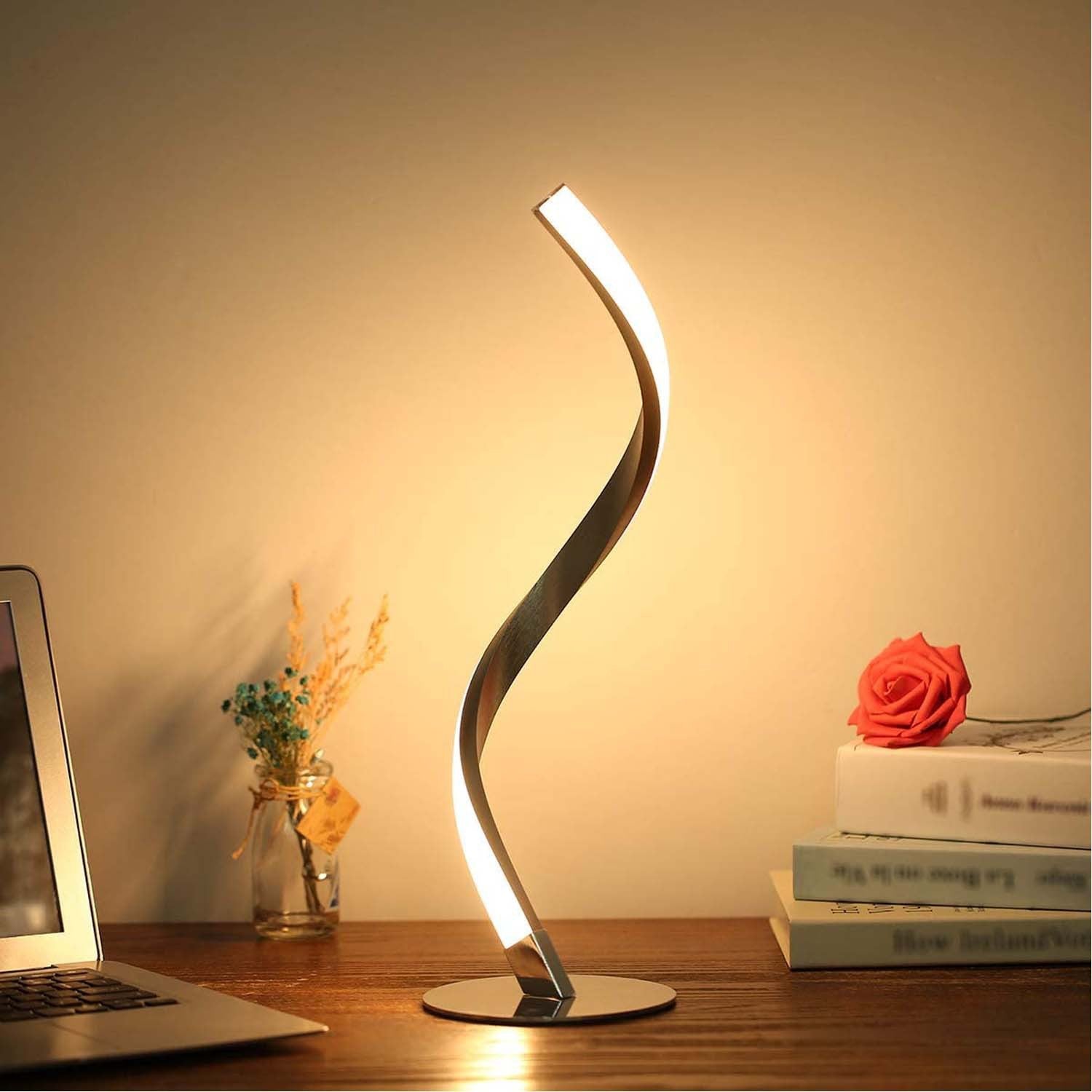 Luxury ambient desk lighting setup featuring the glowing serpentine lamp on a wooden table alongside a laptop and books.