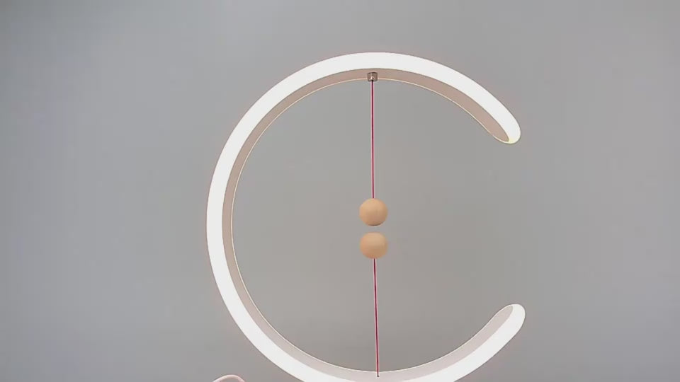 A product demonstration video of the Crescent Magnetic Balance Lamp showing a hand bringing the two wooden magnetic spheres together, causing them to float suspended in mid-air and instantly turn on the warm LED light loop.