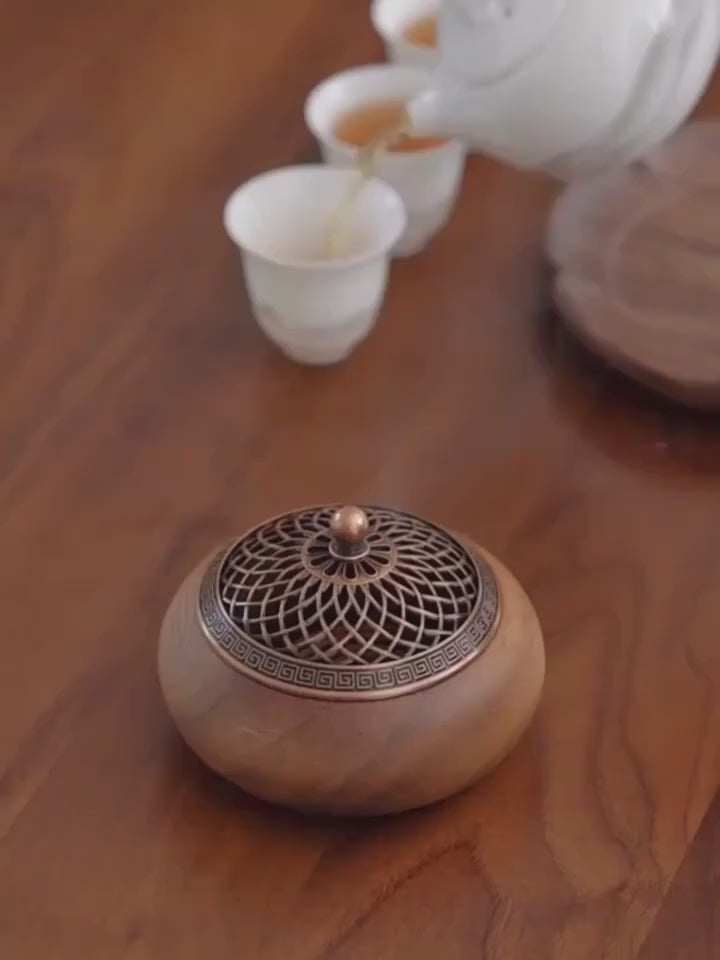 Handcrafted solid wood incense burner with an intricate brass lattice lid, displayed on a wooden table beside a ceramic tea set.