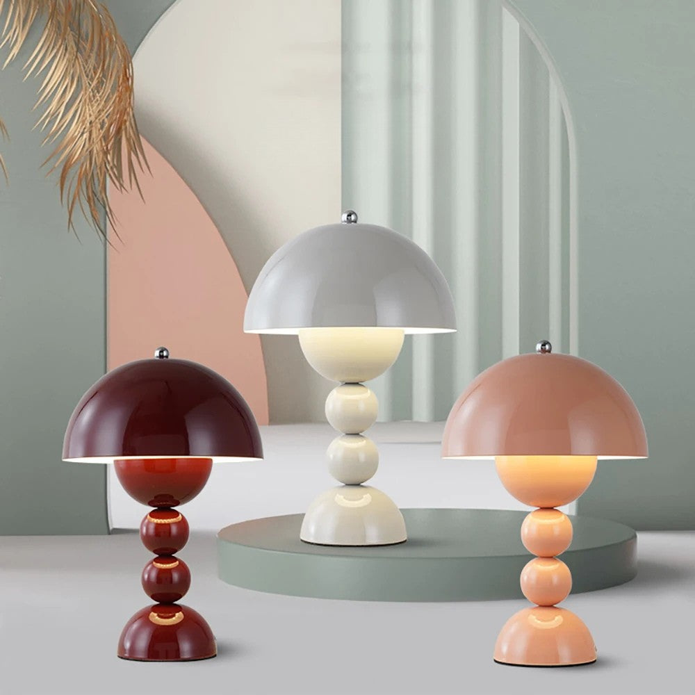 Three Totem sculptural LED table lamps in burgundy, cream white, and peach pink displayed together on a modern green round pedestal.