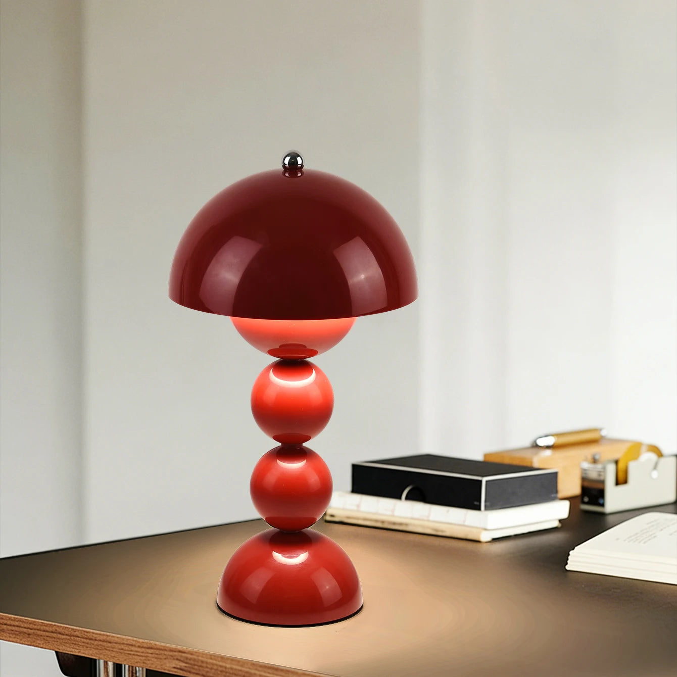 The Totem sculptural red LED table lamp providing a warm ambient glow on a modern wooden office desk next to notebooks and office stationery.
