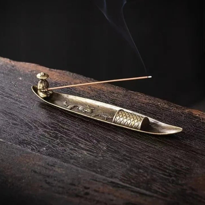 Side view of bronze fisherman boat incense burner with thin trail of smoke.